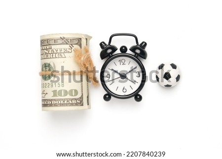 Flatlay picture of alarm clock with miniature ball and fake money. Football business concept.