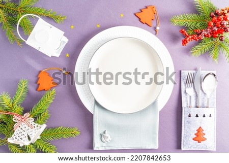 top view of a grey tablecloth with white empty plates surrounded by Christmas trinkets. on the napkin is the symbol of the year 2023 rabbit or hare