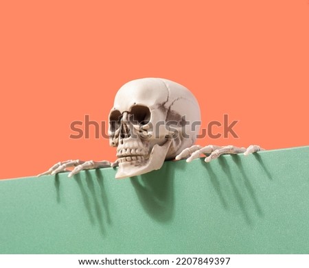 Skeleton on the edge of the table against the two-tone background. Spooky Halloween futuristic concept. Santa Muerte Royalty-Free Stock Photo #2207849397