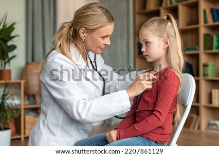 Female doctor checking child's lungs during medical checkup at home interior. Friendly female pediatrician using stethoscope to examine breathing and heartbeat of young patient Royalty-Free Stock Photo #2207861129