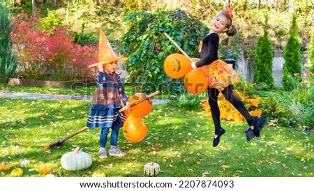 A girl dressed as a witch flies on a broomstick. Fun Halloween party activity ideas. Children joyfully play in the yard on garden brooms with balloons. Photo of a girl on a broom in a jump.