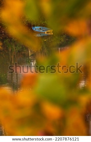 Autumn poetry. Mooring blue boat seen throgh blurry autumn leaves. Autumn landscape at sunset at Marne river in Ile-de-France, France. Beautiful nature, ecology background. Selective focus on boat.