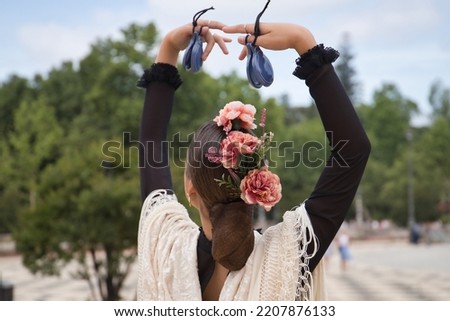 Portrait of young teenage girl in black dance dress, white shawl and pink carnations in her hair, dancing flamenco with castanets in her hands. Concept of flamenco, dance, art, typical Spanish dance. Royalty-Free Stock Photo #2207876133