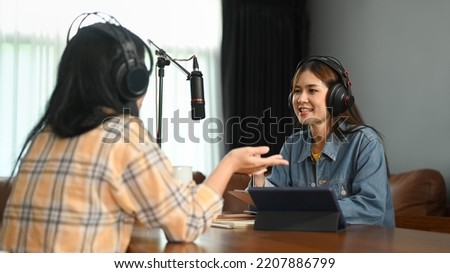 Smiling female radio host discussing various topics with her guest while streaming live audio podcast from home studio