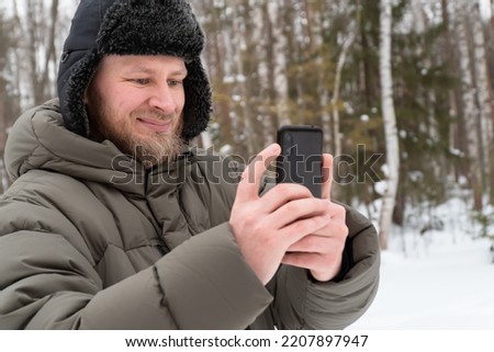 beard man use mobile phone for taking photo walking in winter forest