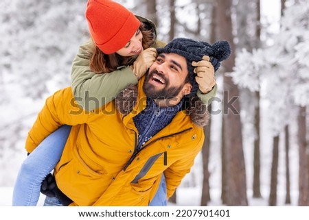 Couple having fun on winter vacation, boyfriend piggybacking girlfriend while spending time outdoors on snowy winter day in mountains