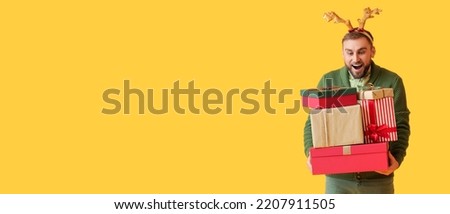 Young man holding Christmas gifts on yellow background with space for text