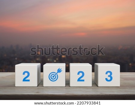 2023 letter with goal icon on white block cubes on wooden table over blur of cityscape on warm light sundown, Happy new year 2023 success concept