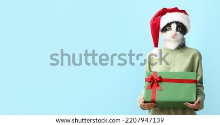 Woman with head of kitten in Santa hat holding Christmas gift on light blue background with space for text
