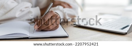Cropped view of african american businesswoman writing on notebook near laptop on table, banner