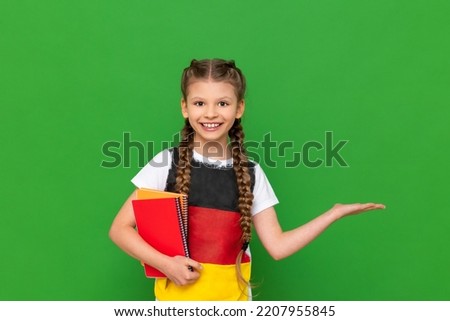A schoolgirl with a German flag on her T-shirt and a textbook in her hands points to the side. German language courses for traveling abroad.