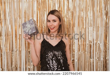 stylish smiling woman in festive dress with gift boxes in her hands against the background of shiny, golden garland