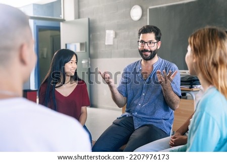 Young friendly teacher listening and talking with teenager students - Group discussion in High School