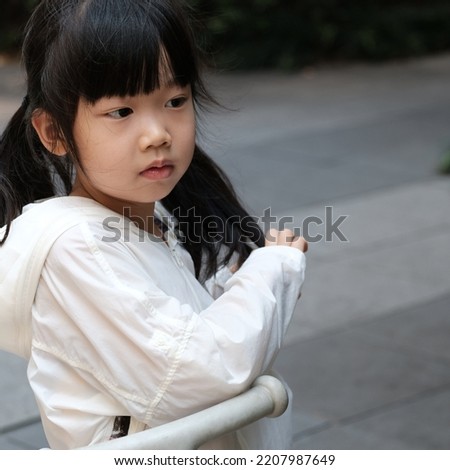 A little Asian girl in white coat leaning on her scooter and playing outdoor. 