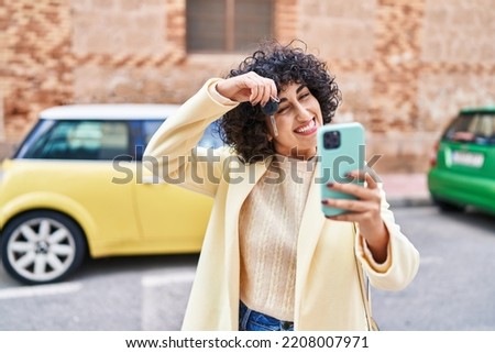 Young middle east woman excutive holding key of new car making selfie by smartphone at street
