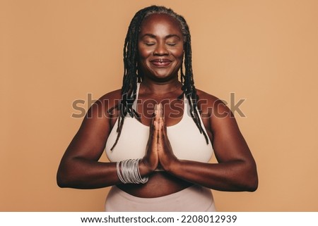 Mature woman meditating with her eyes closed and her hands in prayer position. Black woman with dreadlocks practicing yoga in a studio. Happy middle-aged woman maintaining a healthy lifestyle. Royalty-Free Stock Photo #2208012939