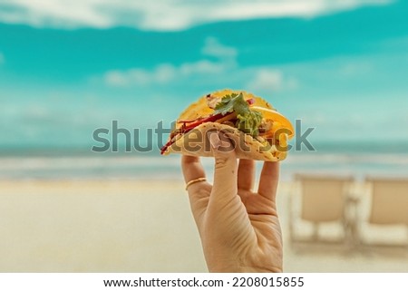 Tasty juicy taco in woman's hand in front of the beach in Tulum, Mexico