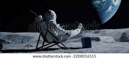 Astronaut sits in a beach chair on a Moon surface, holding phone in hands Royalty-Free Stock Photo #2208016515