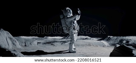 Astronaut searching for cellular or wi-fi signal while walking on Moon surface Royalty-Free Stock Photo #2208016521