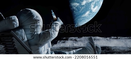 Back view of lunar astronaut having a beer while resting in a beach chair on Moon surface, saluting to Earth Royalty-Free Stock Photo #2208016551