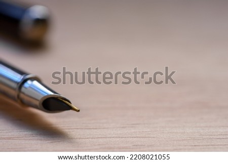 Silver fountain pen on light brown wooden table background.