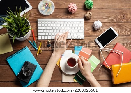 Woman designer typing on keyboard. Creative workspace with color swatches, colorful pencils and cup of coffee. Professional product designing. Coloristics and product branding in visual design studio