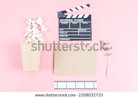 Cinema clapperboard, film strip, craft glass with popcorn, craft leaf and a branch with leaves on a pink background with copy space, top view close-up. Cinema concept.