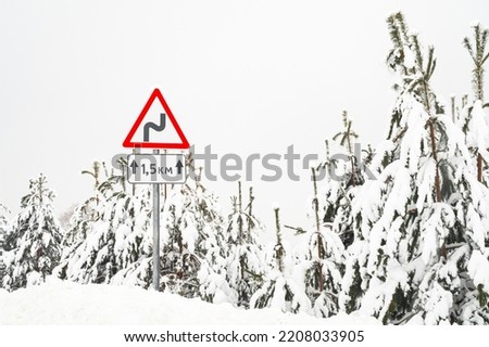 Winter road trip concept. View through the windshield of a car at a warning road sign. Driving on a snowy country road.