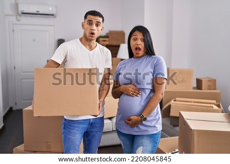 Young hispanic couple expecting a baby moving to a new home in shock face, looking skeptical and sarcastic, surprised with open mouth 