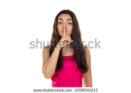 Brunette woman wearing pink top over studio white wall makes silence gesture, keeps finger over lips. Silence and secret concept. 
