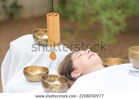 Male hand holding a bamboo Koshi chime musical instrument on sound healing therapy with tibetan singing bowls over young woman during sound massage outdoor, selective focus Royalty-Free Stock Photo #2208050977