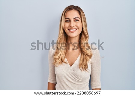 Young blonde woman standing over isolated background with a happy and cool smile on face. lucky person. 