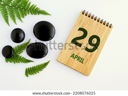 April 29. 29th day of the month, calendar date. Notepad, black stones, green leaves. Spring month, the concept of the day of year.