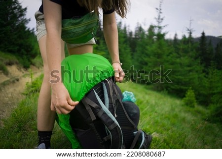 A girl puts a rain cover on her tourist backpack during a hike in the mountains in summer, close-up hands. Royalty-Free Stock Photo #2208080687