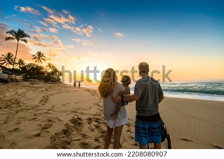 Young family watching a beautiful ocean sunset together at Sunset Beach, Oahu, Hawaii. Beautiful scenic view on a Hawaiian beach. Family moments together