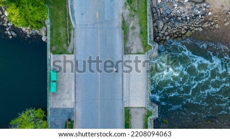 A top down shot, directly above a small two lane road bridge over a creek in the evening, A person is riding a bicycle across it. Shot by a drone camera.