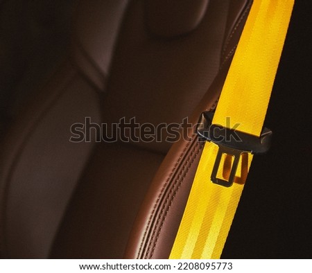 Automobile leather seat of a modern luxury car with a yellow safety belt. Yellow seat belt in a sports car close-up, blurry background. Brown leather car seat. Fasten your seat belts. Royalty-Free Stock Photo #2208095773