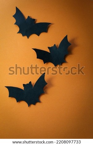 Three black paper bats with an orange halloween background