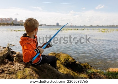 the boy is trying to pull the fish out of the river with the help of a fishing rod, his fishing rod bends from the fish