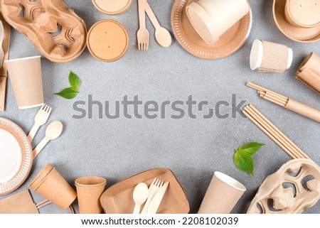 Paper utensils - paper cups, food containers, cup holders, paper straws, plates and wooden bamboo cutlery set over gray concrete background with copy space. Sustainable food packaging concept