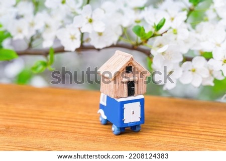 Toy truck carrying a small wooden house on top placed under a blooming branch outdoors.