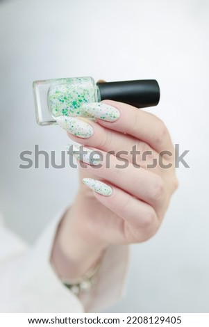 woman hands with long nails light white manicure and a bottle of nail polish