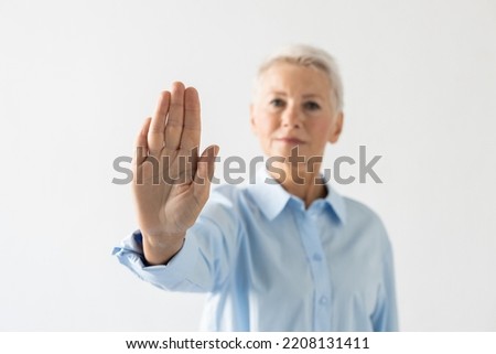 Portrait of senior woman showing stop sign. Female model in blue shirt rejecting something with serious face. Portrait, studio shot, refusal concept