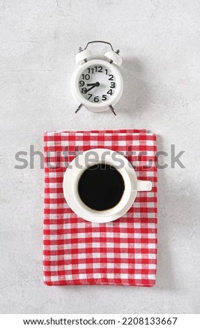 Coffee with alarm clock on light table and red napkin, top view, copy space