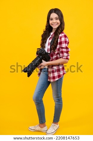 Teenager girl with dslr photo camera with zoom lens. Child photographer isoalted on yellow background. Photo school. Shooting with professional camera. Happy teenager.