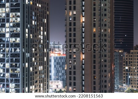 Facades of several big residential houses, high-rises at night with illuminated windows and purple sky in the background; elevation of dwelling skyscrapers with dark and bright windows and balconies Royalty-Free Stock Photo #2208151563