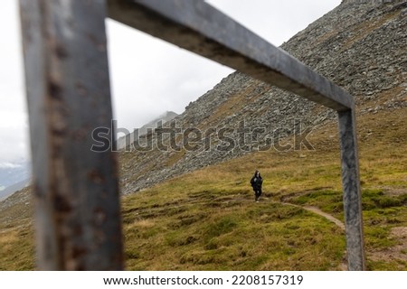 A woman in a rain cape climbs a mountain path, a picture in a metal frame. Austria, Alps