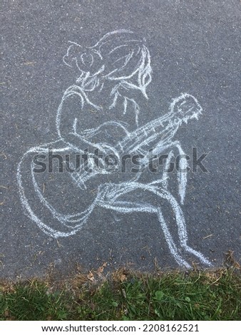 Drawing with chalk outside on the sidewalk. A girl with a guitar. Painting in nature. A cartoon picture of a guitarist playing.