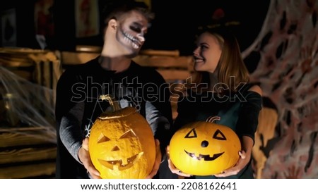 date in style of Halloween party, night, twilight, in the rays of light, guy with a girl dressed in costumes and with a terrible makeup are holding two large Halloween pumpkins. High quality photo