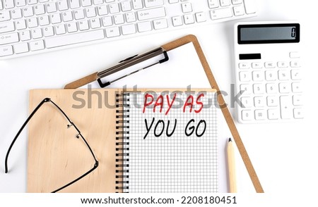 Notebook with the word PAY AS YOU GO with keyboard and calculator on white background